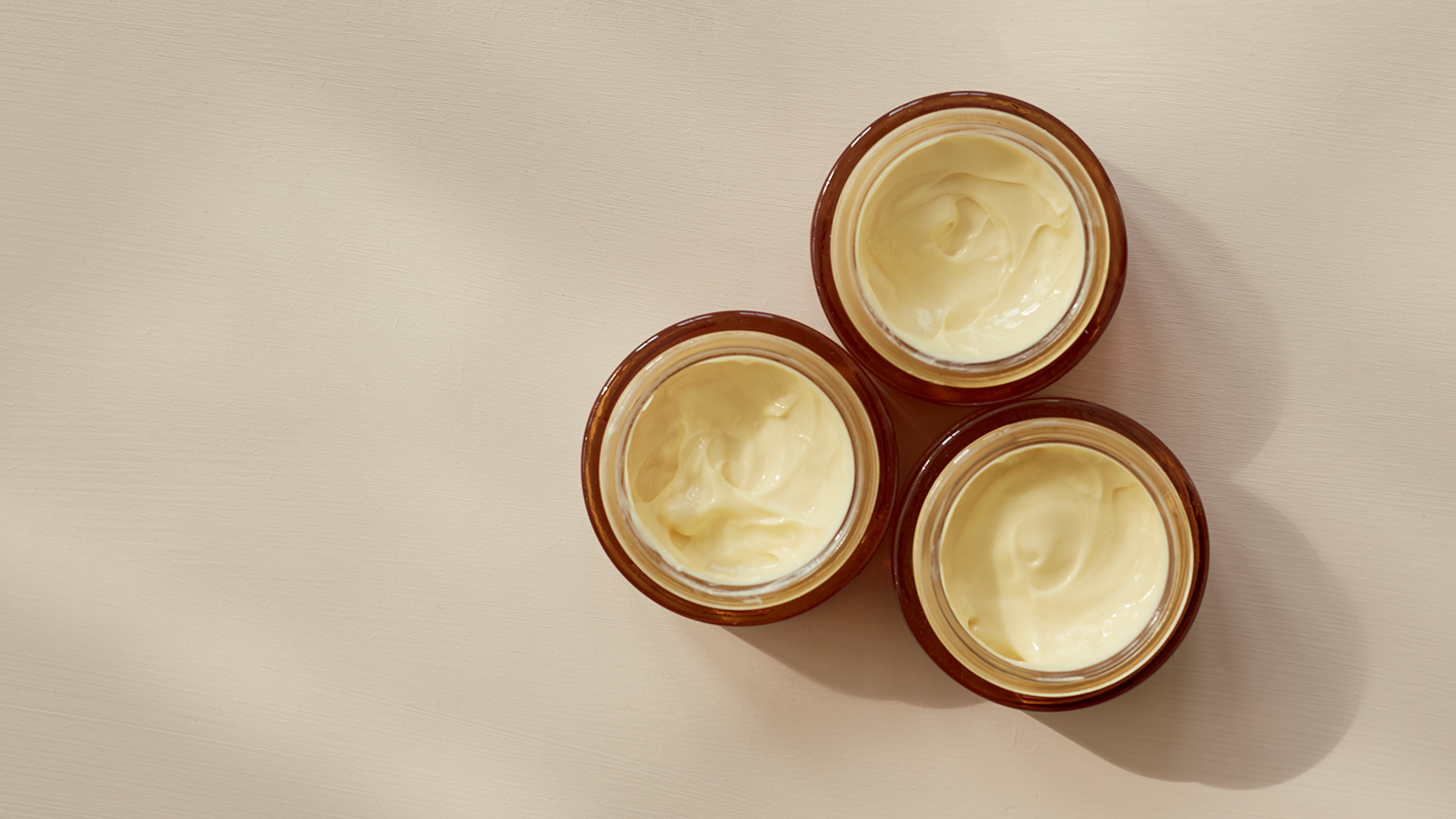 Astaxanthin – naturens røde guld til smuk og ungdommelig hud 12 Tre åbne krukker med lys creme set ovenfra på en lys baggrund.
