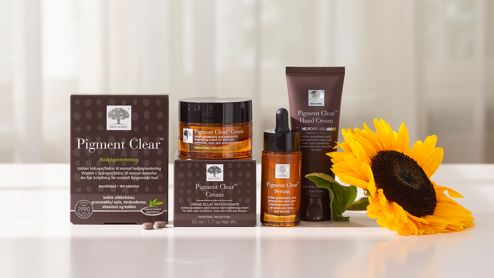 Hvad gør Pigment Clear™-hudplejeserien unik? 5 New Nordic Pigment Clear™ hudplejeserie med creme, serum, håndcreme og kosttilskud ved en solsikke.